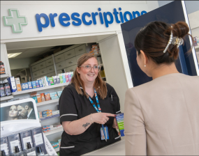 Image of a pharmacy worker behind a counter talking to a customer.