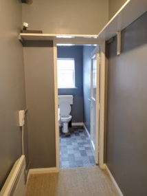 A photo of a carpeted hallway, with painted walls and a radiator, leading to a bathroom