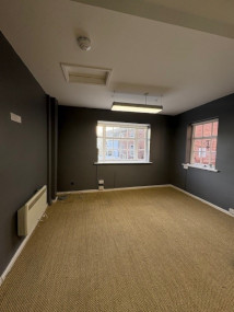 A photo in the office space, with carpeted floor, overhead lighting, a radiator and two external windows