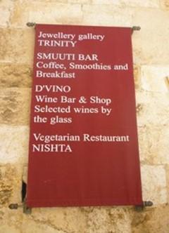 A red banner on a stone wall in Dubrovnik, a UNESCO World Heritage city, lists several businesses located in a narrow lane. The banner advertises multiple businesses from top to bottom.