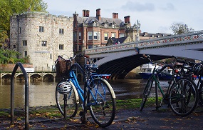 A blue bicycle is parked on a bike rack with Lendal Bridge in the background

Caption: Cycle parking at Lendal Bridge