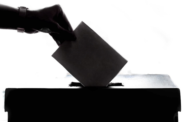 Silhouette of a hand posting a vote into a ballot box.