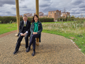 A man and woman sit on a wooden frame in front of houses
