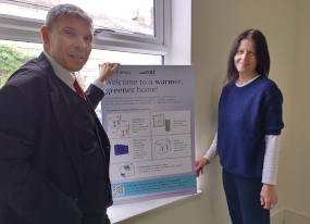 A man and a woman in a room hold a poster of energy efficiency information
