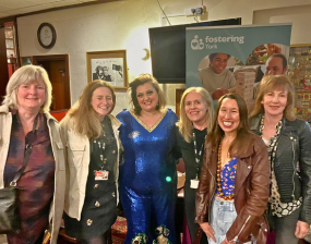 A group of people stand smiling and looking at the camera, the comedian Kiri Pritchard McLean stands in the middle in a blue sequined outfit