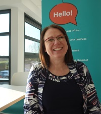 Monica, from Partner PR infront of a teal banner smiling.