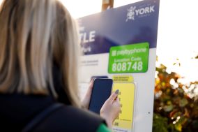 The back of a woman is shown who's holding a phone to pay car parking