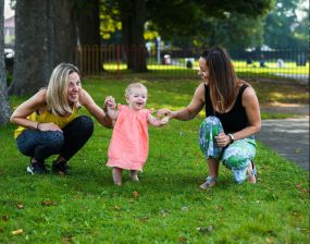 photo of two women helping a small child to walk